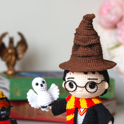 Harry Potter amigurumi crochet toy pattern in black cloak with red and yellow Gryffindor scarf, blue H letter sweater  and crocheted Hedwig owl. And the Sorting Hat crochet amigurumi pattern from Harry Potter, featuring detailed folds and a face, made with brown yarn